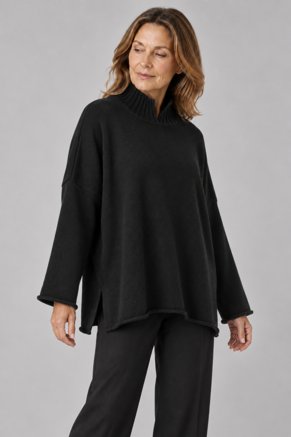oversized jumper featuring long sleeves, a high ribbed neckline, and a center front opening, presented in a black colour, viewed from the front, presented by middle age woman model wearing graphite colour trouser
