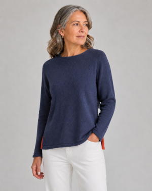 Older woman with gray hair wearing a navy knit sweater and white pants, looking to the right.