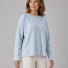 Kitty cashmere blend relaxed jumper with drop shoulders, longer back hem and ribbed back panel detail in soft luxury knit in chalk blue colour, presented by lady with long brown hair and white trousers