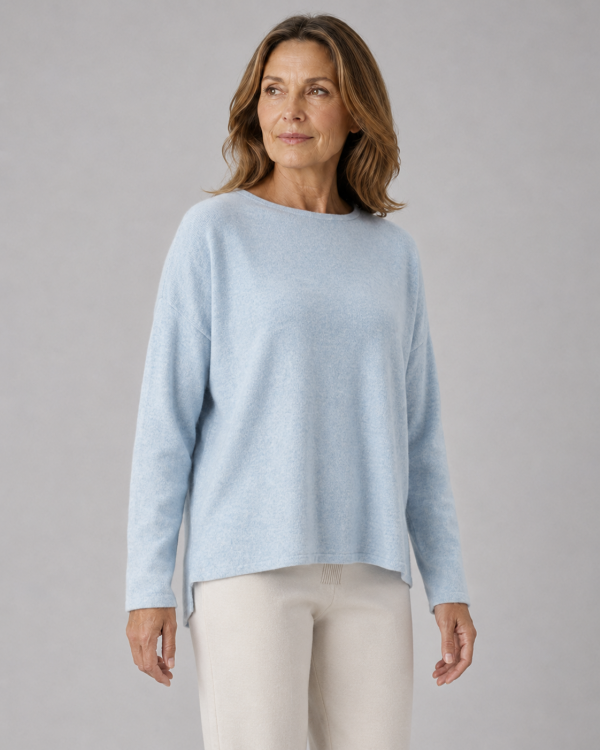 Kitty cashmere blend relaxed jumper with drop shoulders, longer back hem and ribbed back panel detail in soft luxury knit in chalk blue colour, presented by lady with long brown hair and white trousers