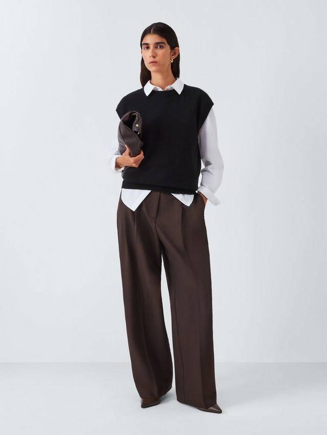 Model wearing a black sleeveless top over a white shirt with brown wide-leg trousers, holding a clutch office-ready look.