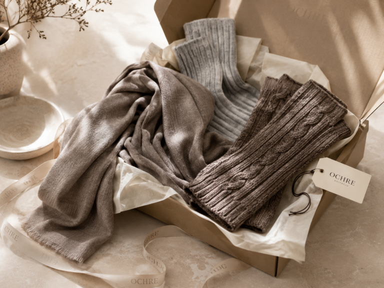 Best knitwear gifts for women displayed in an Ochre gift box with a Fine Scarf, Long Cable Fingerless Gloves and Ribbed Socks in a soft winter editorial setting.