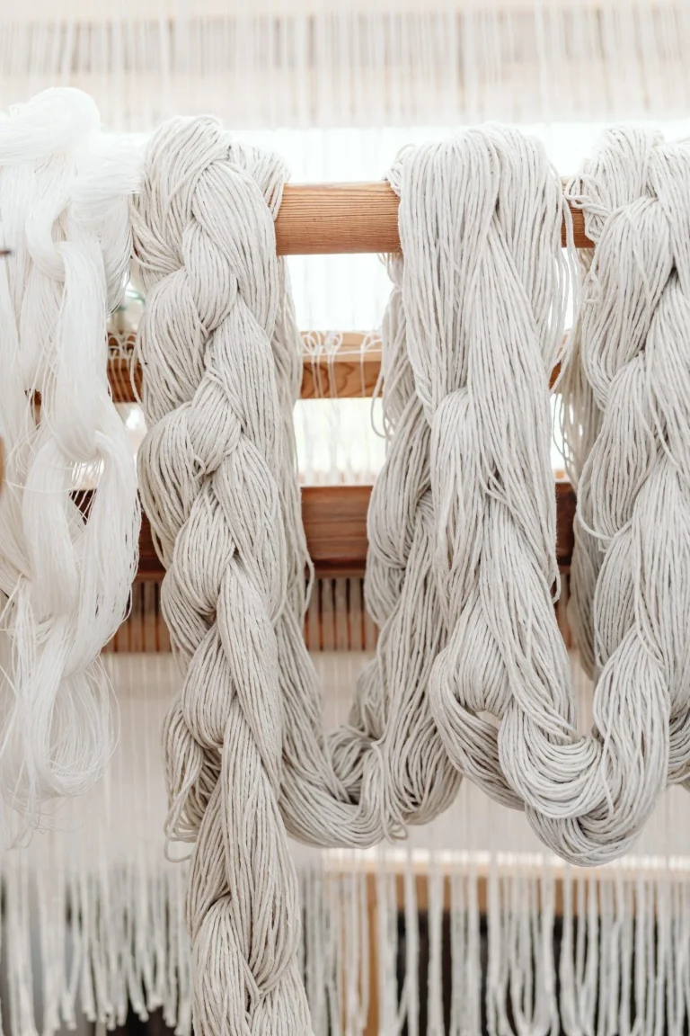 Cream-colored yarn skeins draped over a wooden loom in a weaving studio