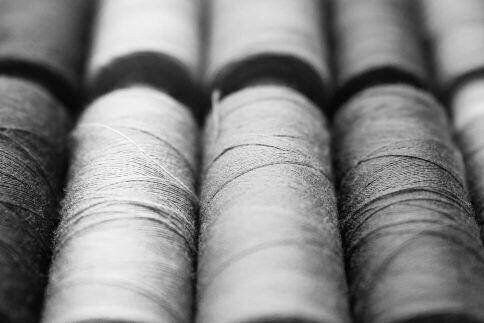 Close-up of numerous grey thread spools arranged in parallel rows in grayscale.
