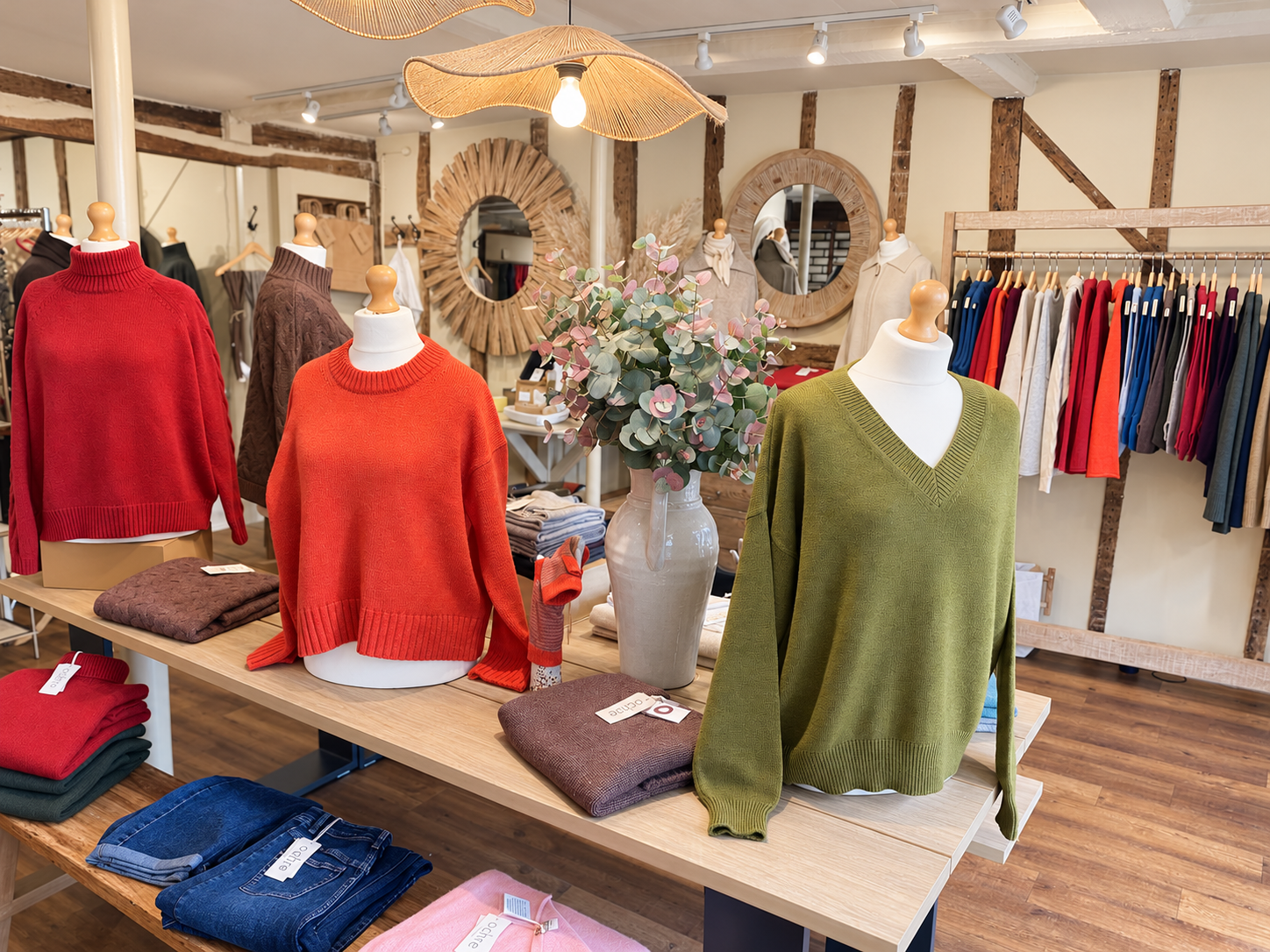 Red, orange and green jumpers on mannequins above a wooden display table at Ochre’s knitwear shop in Lewes.